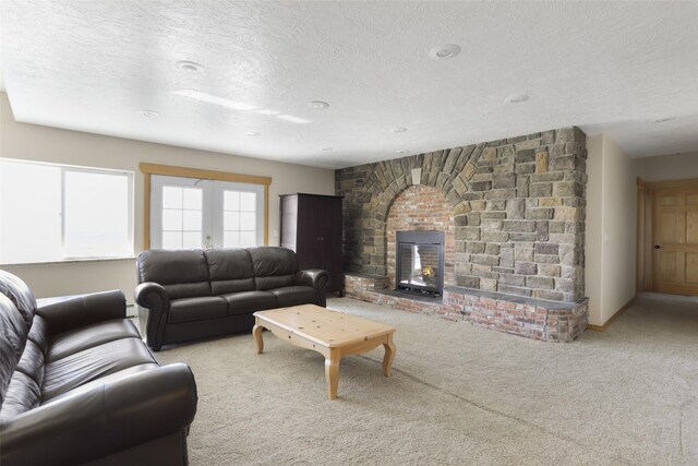 carpeted living room with a stone fireplace, french doors, and a textured ceiling