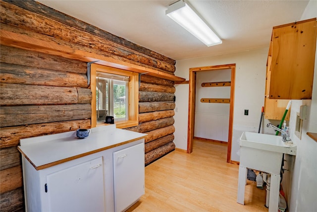 kitchen with baseboards, light countertops, light wood finished floors, and white cabinetry