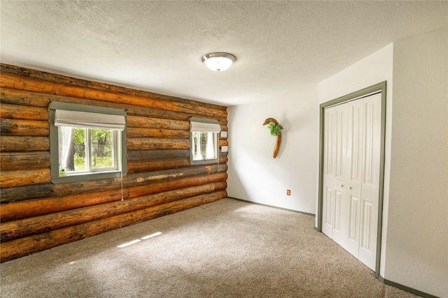 carpeted spare room with a wealth of natural light, rustic walls, and a textured ceiling