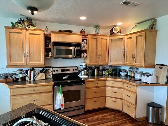 kitchen with light brown cabinetry, dark hardwood / wood-style floors, stainless steel appliances, and a textured ceiling