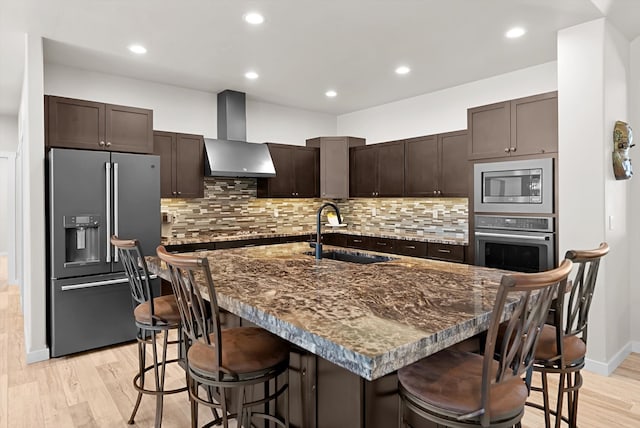 kitchen with light hardwood / wood-style flooring, stainless steel appliances, a kitchen breakfast bar, sink, and wall chimney exhaust hood