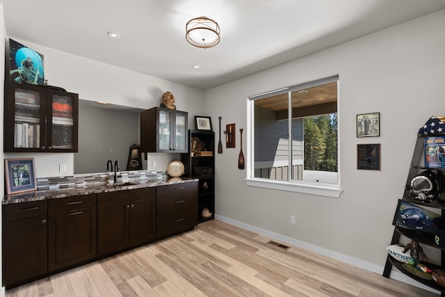 kitchen with backsplash, light hardwood / wood-style flooring, sink, dark brown cabinets, and dark stone counters