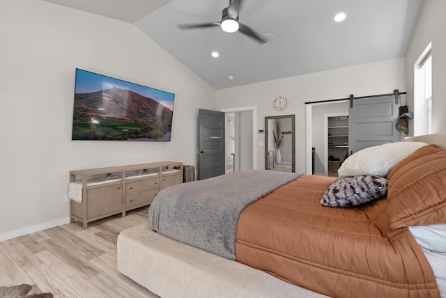 bedroom with light hardwood / wood-style flooring, a barn door, lofted ceiling, a spacious closet, and ceiling fan