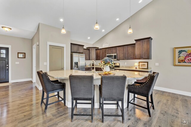 kitchen with appliances with stainless steel finishes, high vaulted ceiling, a spacious island, a kitchen bar, and decorative light fixtures