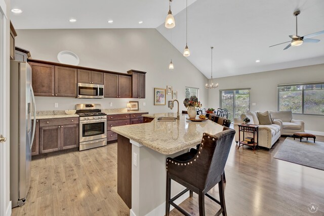 kitchen featuring a breakfast bar, sink, light stone counters, decorative light fixtures, and appliances with stainless steel finishes