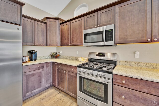 kitchen featuring vaulted ceiling, light stone counters, stainless steel appliances, dark brown cabinets, and light hardwood / wood-style flooring