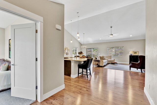 interior space with lofted ceiling, hanging light fixtures, light wood-type flooring, a kitchen breakfast bar, and an island with sink