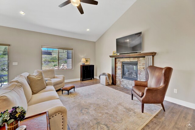 living room featuring a stone fireplace, light hardwood / wood-style flooring, ceiling fan, and vaulted ceiling