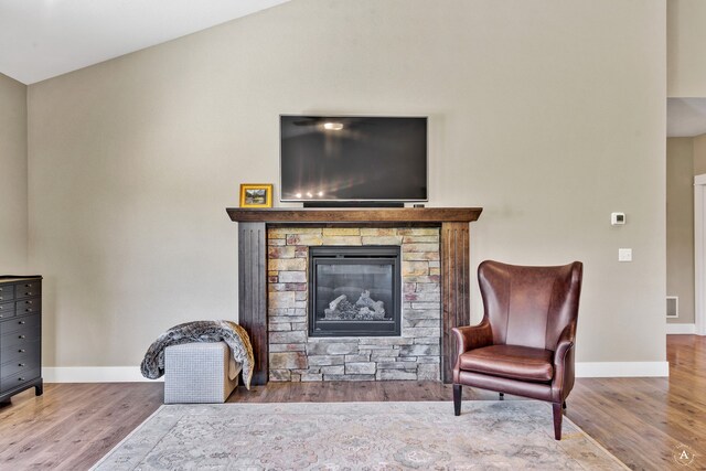 sitting room featuring lofted ceiling, wood-type flooring, and a stone fireplace