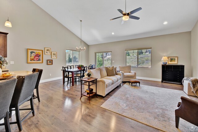 living room with ceiling fan with notable chandelier, wood-type flooring, and high vaulted ceiling