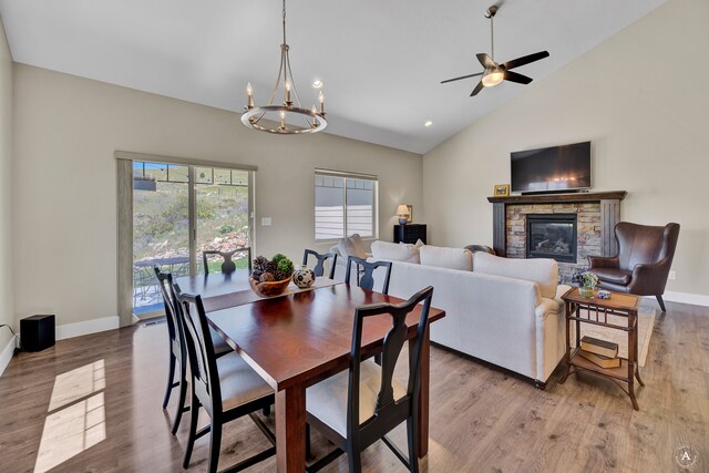 dining space with hardwood / wood-style flooring, a fireplace, ceiling fan with notable chandelier, and vaulted ceiling