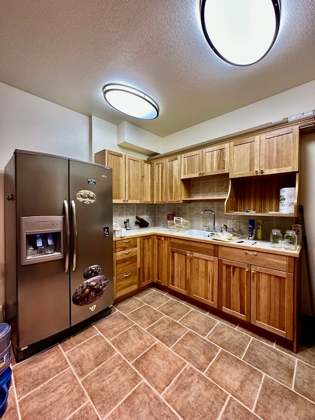 kitchen featuring backsplash, stainless steel fridge, sink, and a textured ceiling