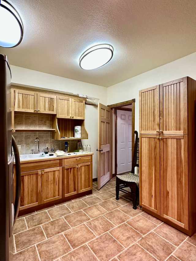 kitchen featuring backsplash, stainless steel refrigerator, sink, and a textured ceiling