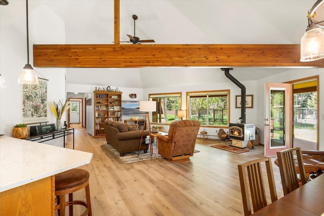 living room featuring beam ceiling, a wood stove, ceiling fan, light hardwood / wood-style flooring, and high vaulted ceiling