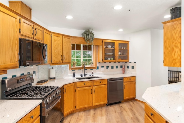 kitchen featuring light wood-type flooring, backsplash, light stone counters, sink, and black appliances