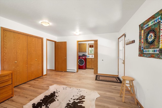 bedroom with a closet, light wood-type flooring, a baseboard heating unit, and washer / dryer