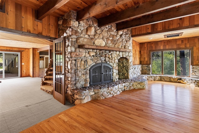 unfurnished living room featuring light hardwood / wood-style flooring, a fireplace, beam ceiling, wood ceiling, and wooden walls