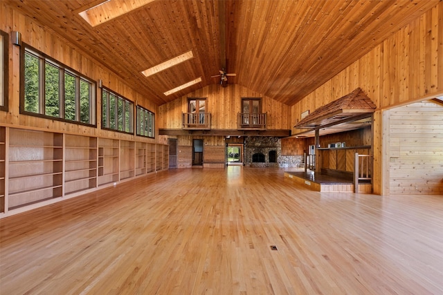 interior space with a stone fireplace, light hardwood / wood-style floors, wooden ceiling, and a skylight