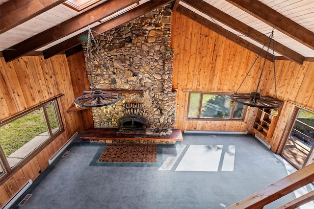 unfurnished living room featuring beamed ceiling, high vaulted ceiling, a healthy amount of sunlight, and wood walls