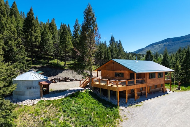 rear view of house featuring metal roof, a standing seam roof, gravel driveway, and a forest view