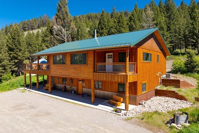 view of front facade with a balcony, metal roof, cooling unit, a patio area, and a wooded view