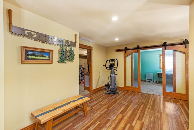 workout room featuring recessed lighting, visible vents, a barn door, wood finished floors, and baseboards