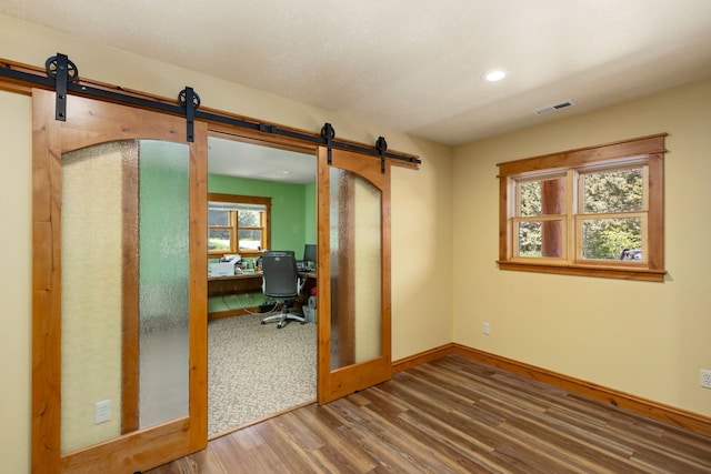 office space featuring a barn door, recessed lighting, wood finished floors, visible vents, and baseboards