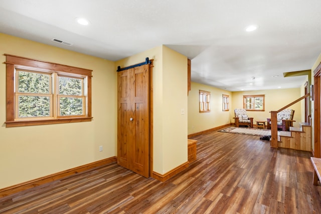 interior space featuring a barn door, recessed lighting, wood finished floors, visible vents, and baseboards