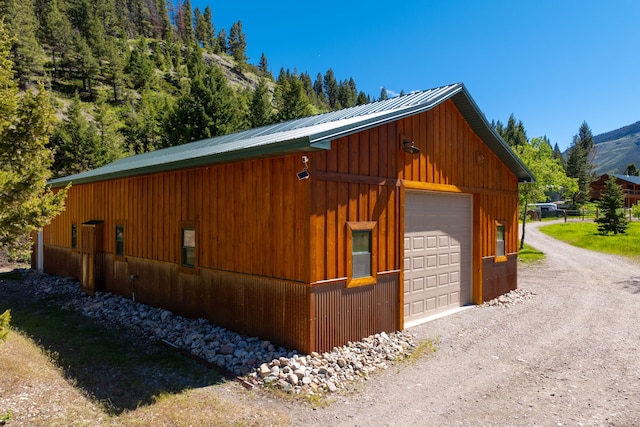 view of side of property featuring dirt driveway, a detached garage, metal roof, an outbuilding, and a mountain view