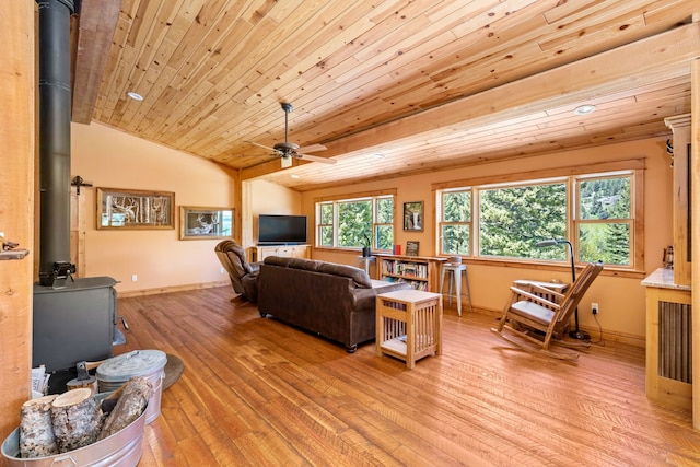 living area featuring light wood-type flooring, a wood stove, lofted ceiling, and baseboards