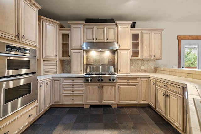 kitchen featuring tasteful backsplash, tile counters, light brown cabinetry, and appliances with stainless steel finishes