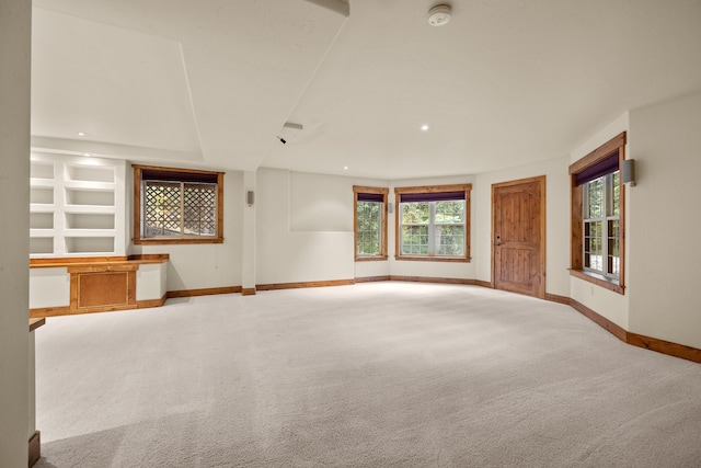 unfurnished living room featuring light carpet and built in shelves