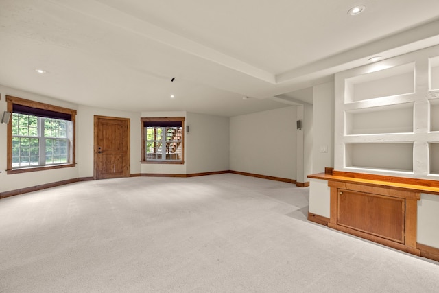 unfurnished living room with a healthy amount of sunlight, built in features, and light carpet