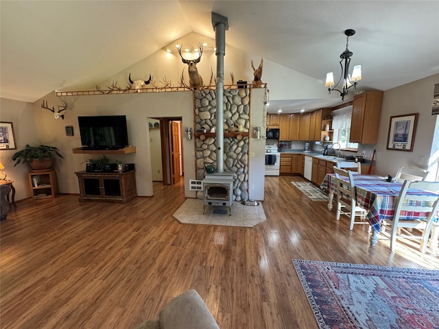 interior space featuring a wood stove, white appliances, hardwood / wood-style flooring, vaulted ceiling, and sink