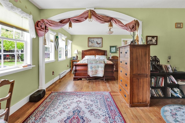 bedroom with multiple windows, light hardwood / wood-style floors, and a baseboard heating unit