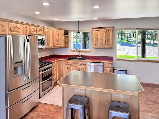 kitchen with a kitchen island, a sink, a kitchen breakfast bar, hanging light fixtures, and appliances with stainless steel finishes