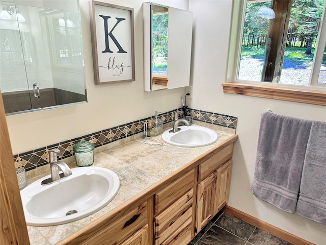 full bathroom with double vanity, a stall shower, a sink, and baseboards