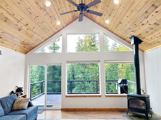 living area with high vaulted ceiling, wooden ceiling, wood finished floors, baseboards, and a wood stove