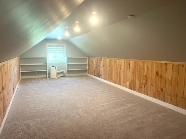 additional living space featuring wooden walls, light carpet, and lofted ceiling