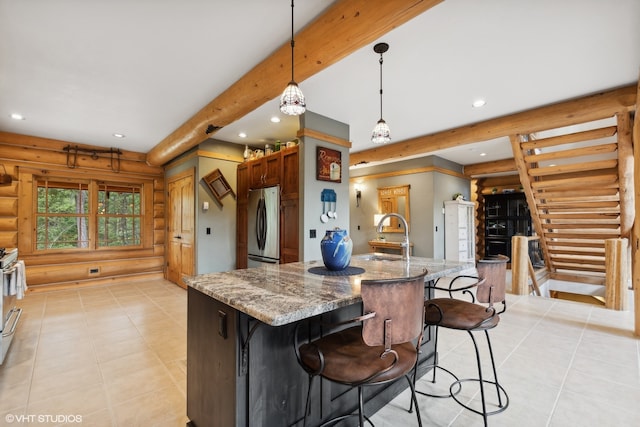 kitchen featuring stone counters, sink, stainless steel fridge, pendant lighting, and a kitchen island with sink