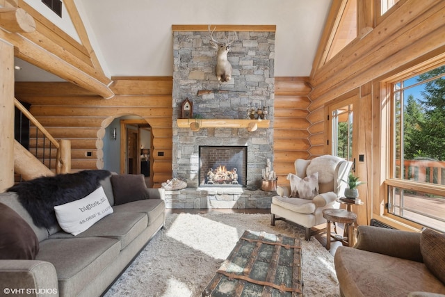 living room with log walls, a stone fireplace, beamed ceiling, and high vaulted ceiling