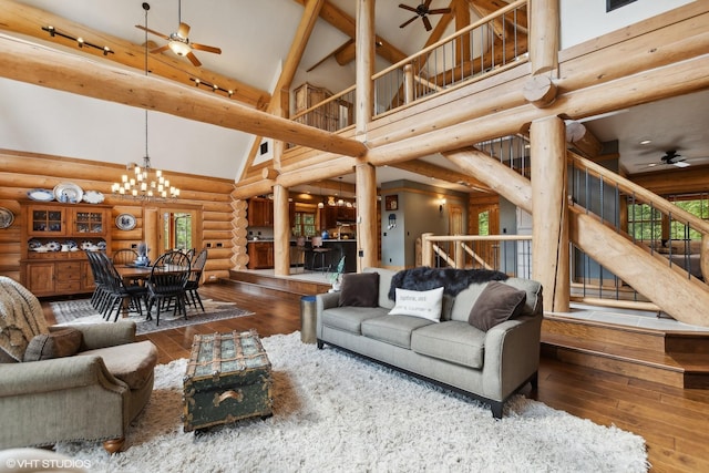 living room with hardwood / wood-style floors, high vaulted ceiling, ceiling fan with notable chandelier, rustic walls, and beamed ceiling