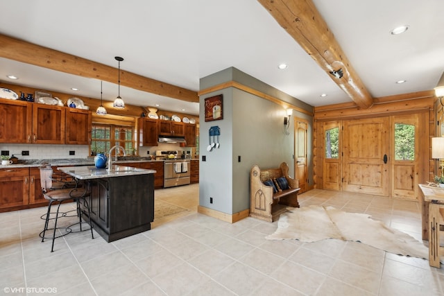 kitchen with a breakfast bar, backsplash, a center island with sink, beam ceiling, and stainless steel range oven