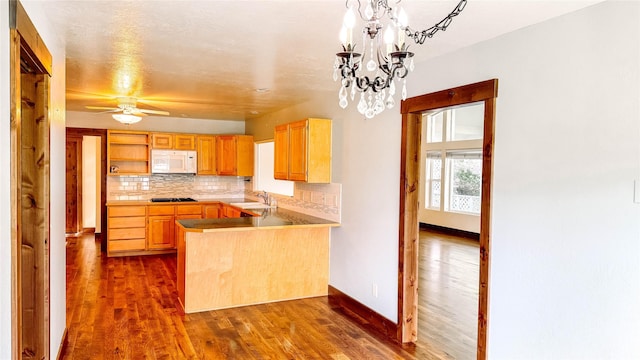 kitchen featuring pendant lighting, backsplash, dark hardwood / wood-style flooring, kitchen peninsula, and black gas stovetop