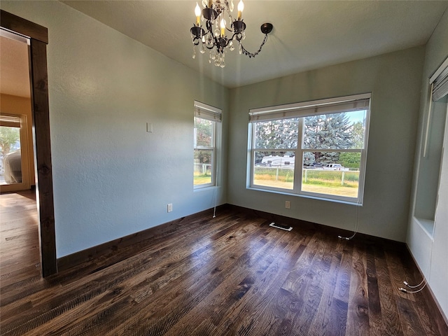 spare room featuring dark wood-type flooring and a chandelier