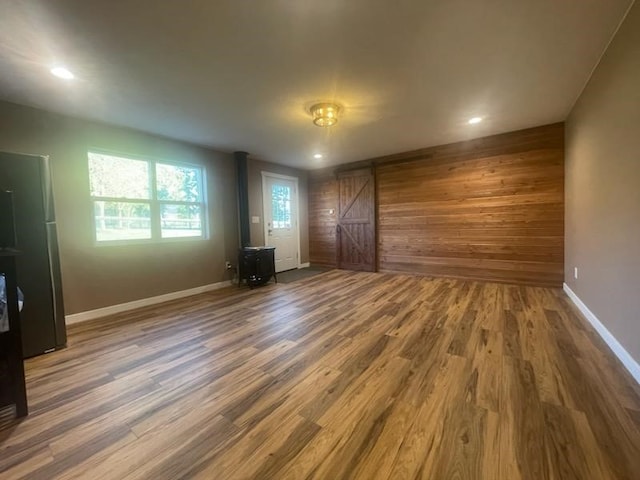 unfurnished living room with hardwood / wood-style floors, wooden walls, and a barn door