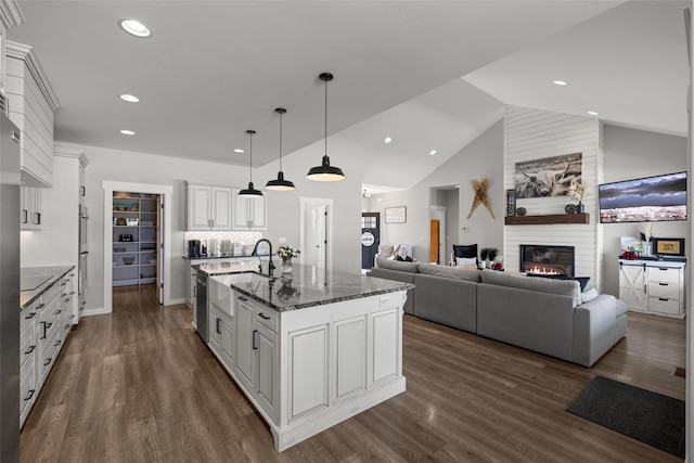 kitchen with white cabinetry, dark stone countertops, decorative backsplash, hanging light fixtures, and a center island with sink