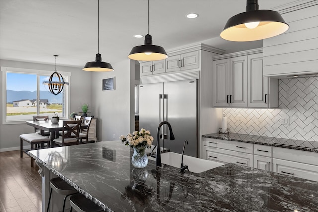 kitchen featuring decorative light fixtures, stainless steel built in refrigerator, sink, dark stone counters, and decorative backsplash