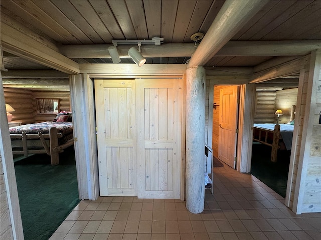 interior space featuring beamed ceiling, track lighting, wood ceiling, and rustic walls