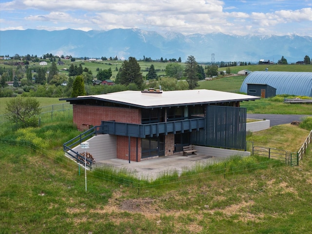 rear view of house with a rural view, a mountain view, brick siding, an outdoor structure, and an exterior structure